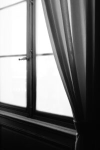 A vertical grayscale shot of an old window and a curtain next to it with white background